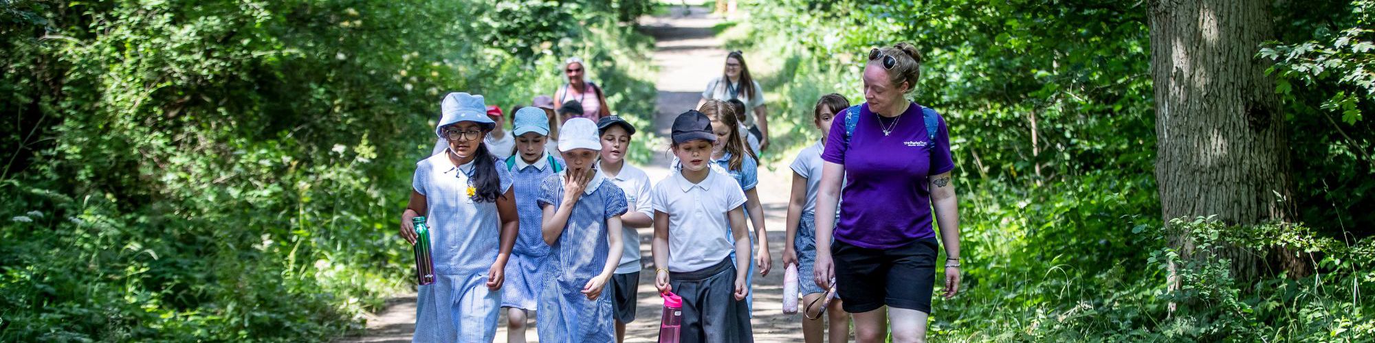 Outdoor learning leader and primary school group walking through Milton Keynes woodland