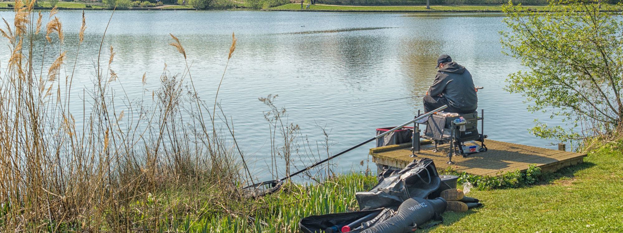 person sat down at a lake with their fishing gear