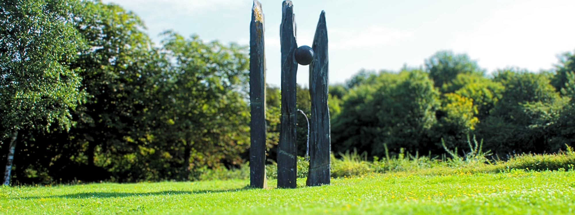 this stone structure has 3  varying vertical rectangular poles however between the 2nd a 3rd pole a large stone ball has been merged into the gap between the poles 