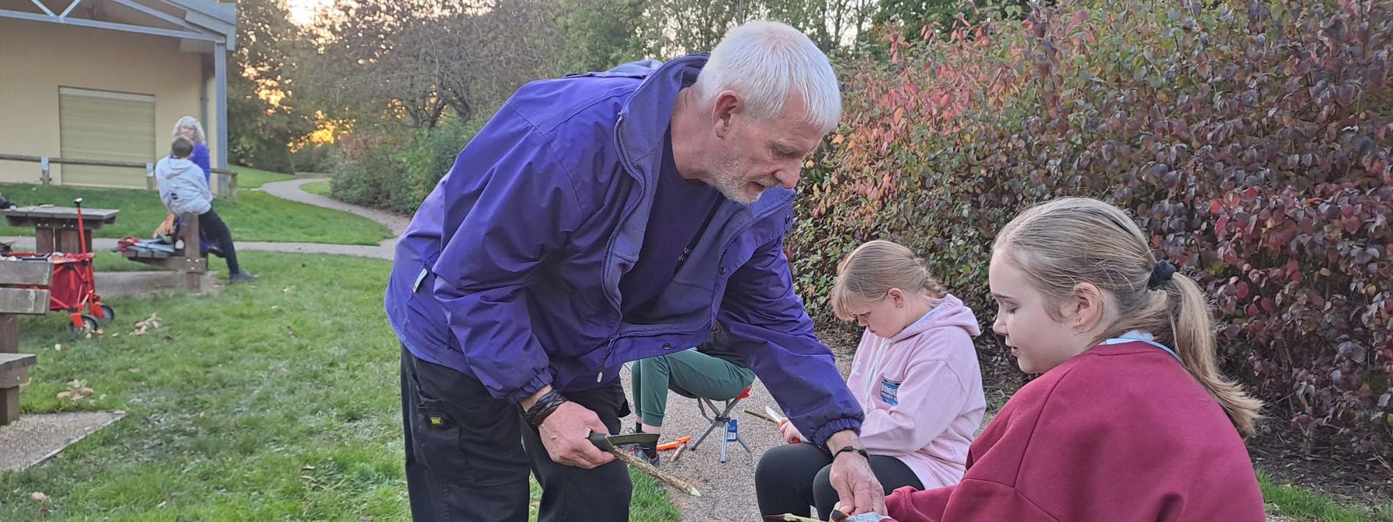 Parks Trust volunteer helping children with a whittling session in the park