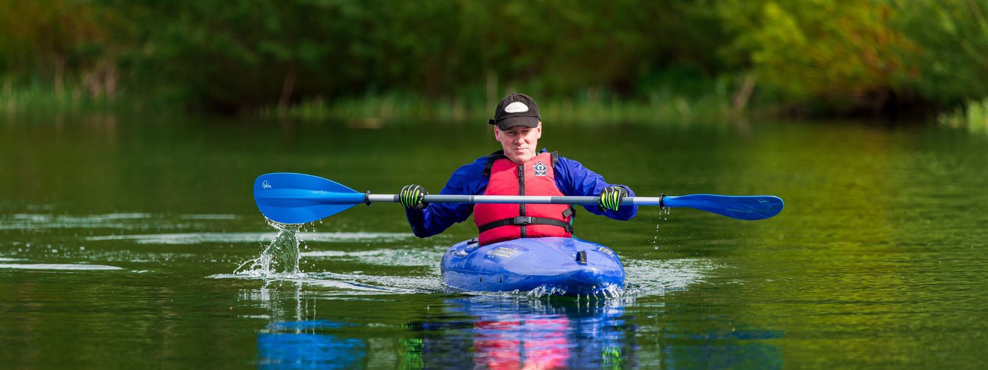 Person in blue kayak on lake with paddleboard