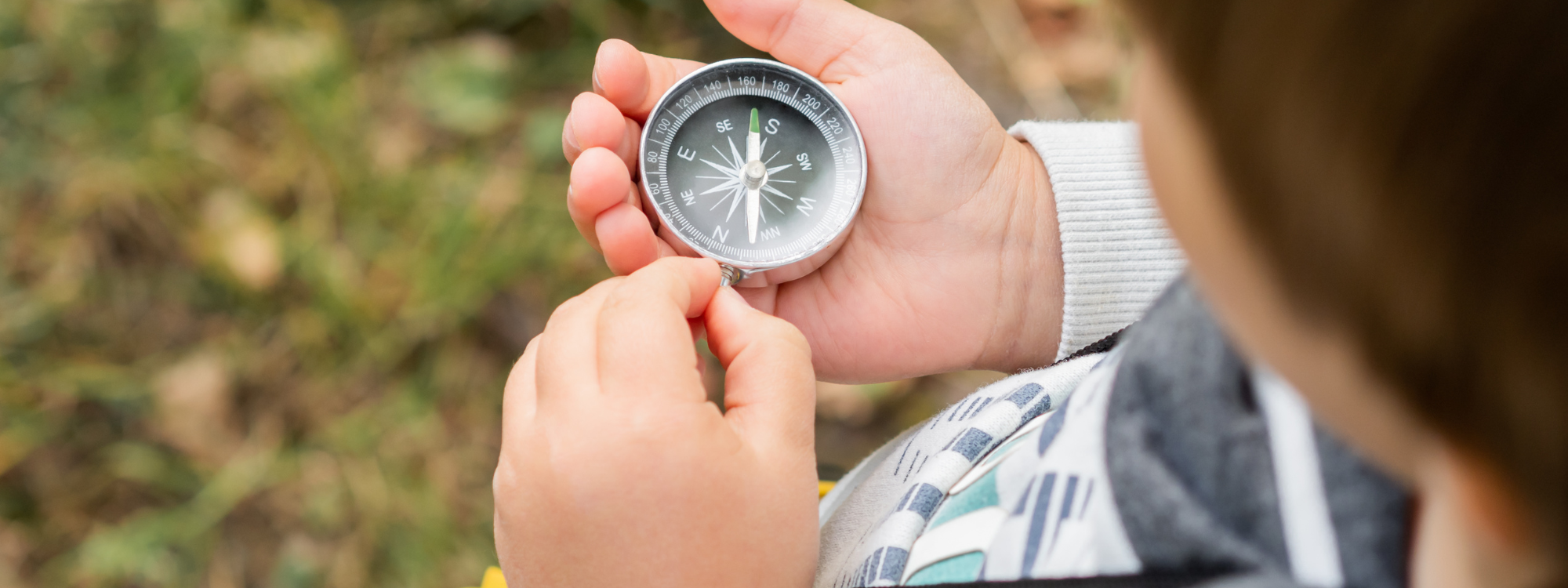 A young child holding a metal compass in their hand and looking at it