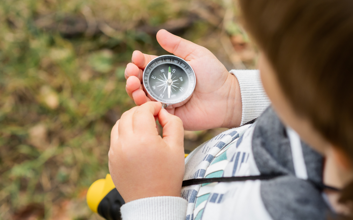 A young child is look at a metal compass that they are holding in their hand.