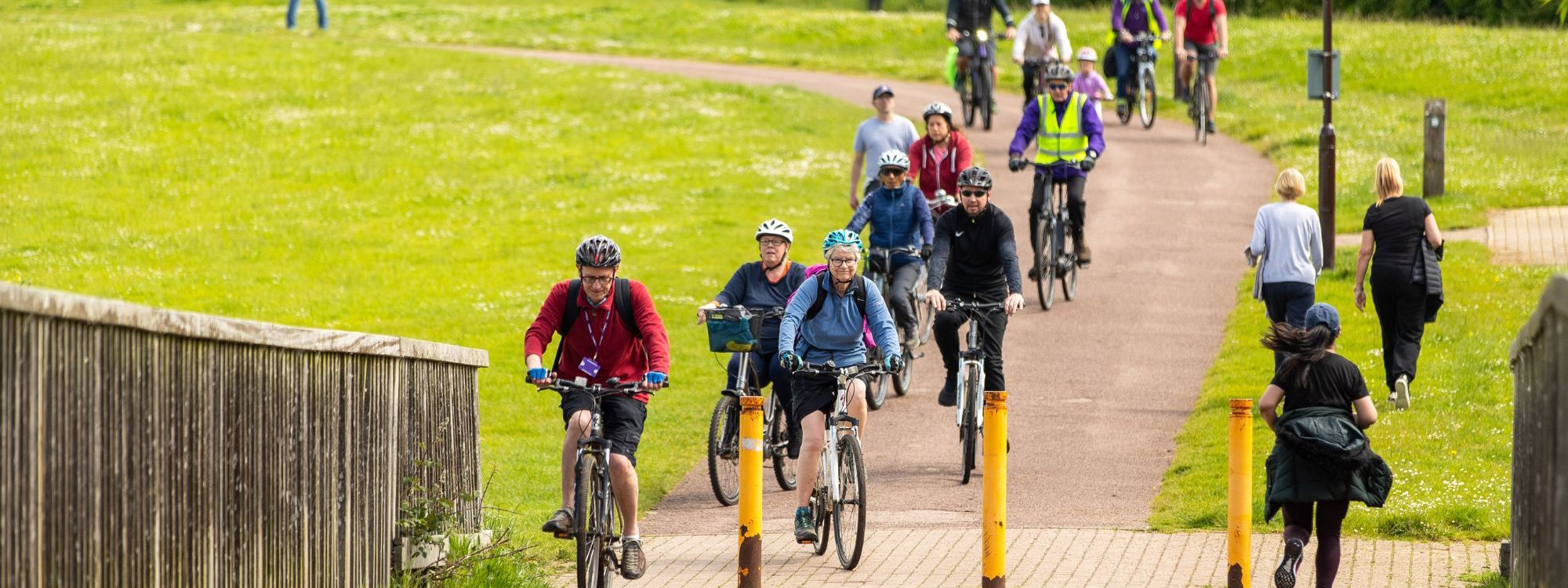 Group of people on a bike ride at Furzton Lake, coming down the hill over bridge