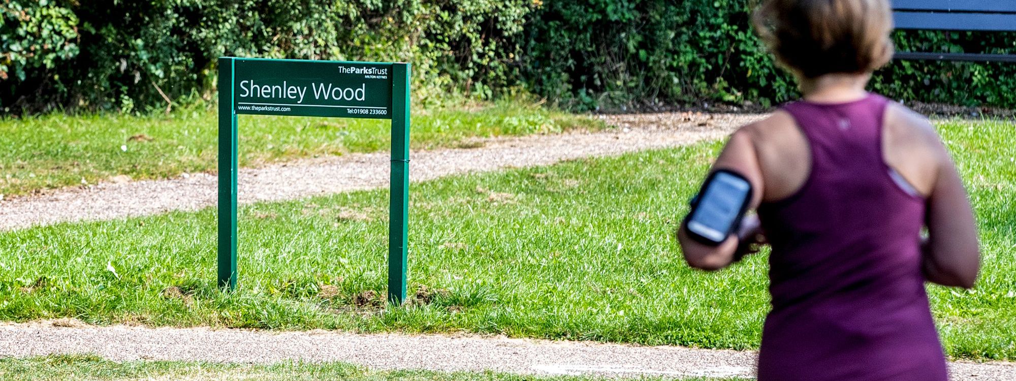 Person running past Shenley Wood sign in the park