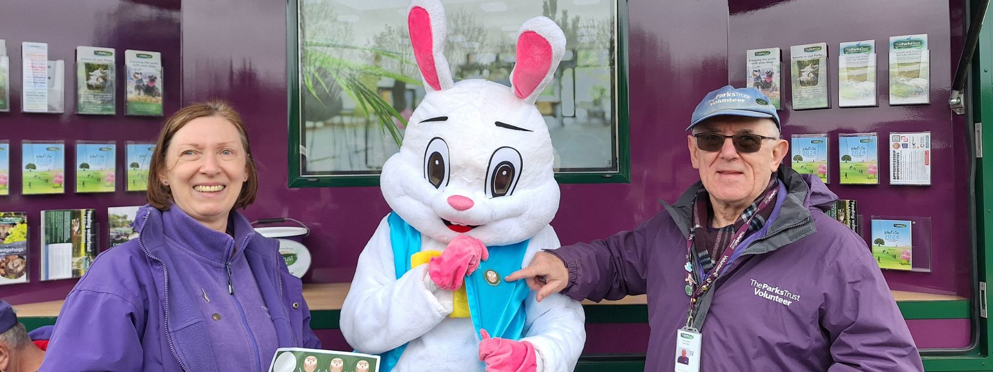 Happy Easter Bunny with light blue jacket and yellow bow tie picture between two Parks Trust Volunteers 