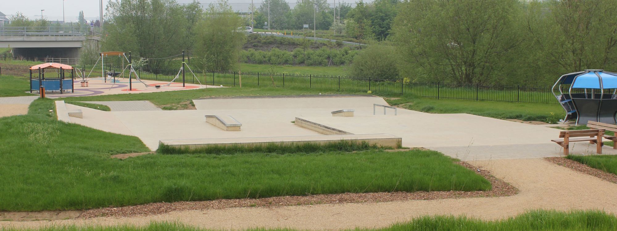 Skate park surrounded by grass and green trees on a cloudy day