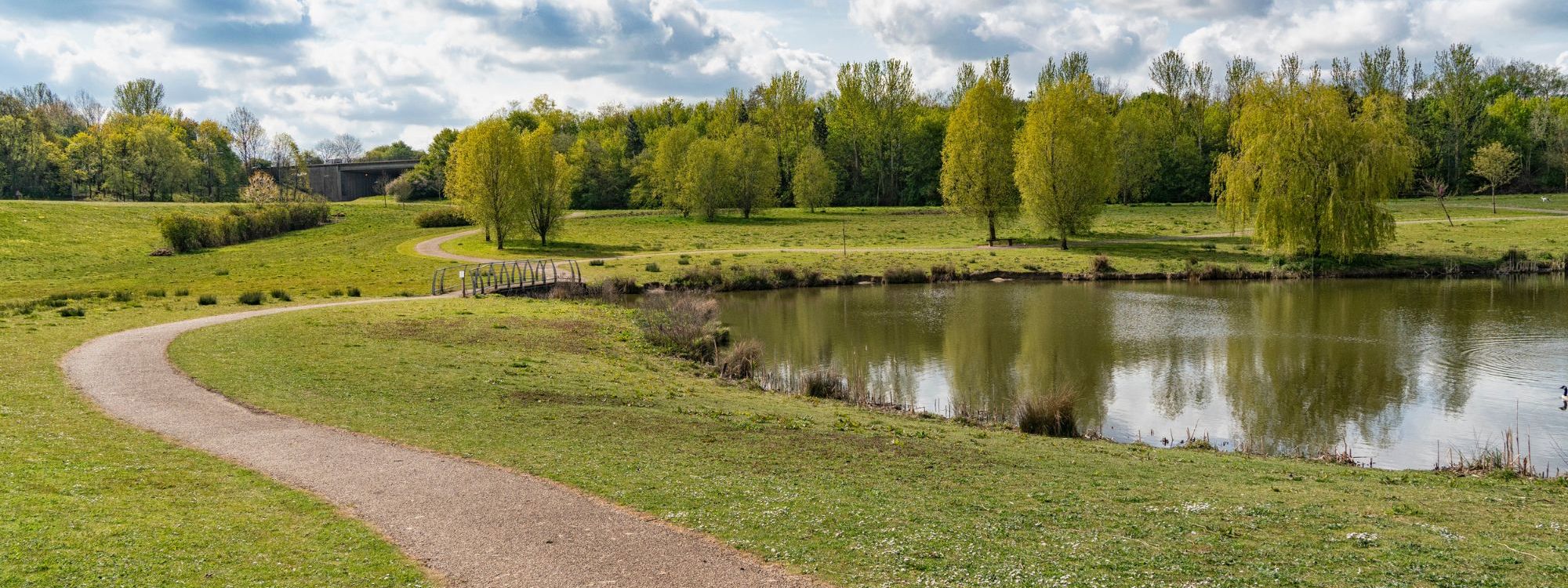 Pathway along Milton Keynes lake with blue sky and clouds