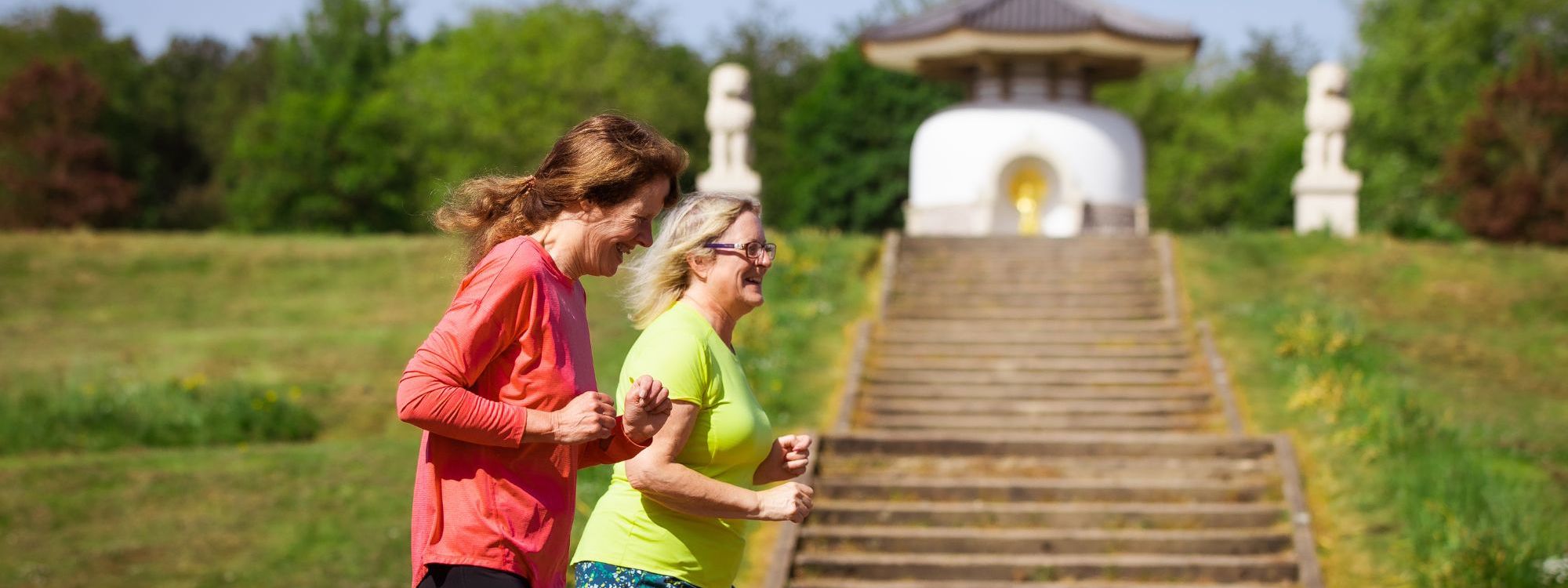 Two people running together at Willen Lake North with Peace Pagoda in the background