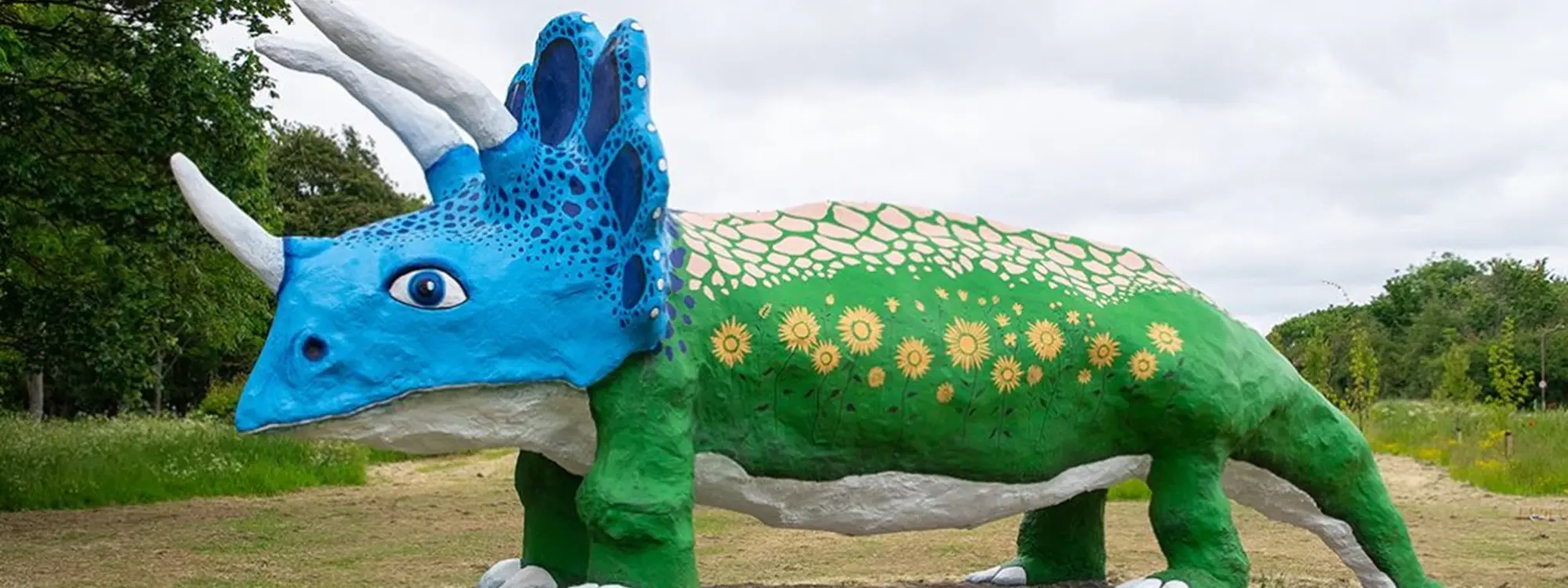 large triceratops the body is painted green with sunflowers dotted round which are yellow and the dinosaur has a blue head