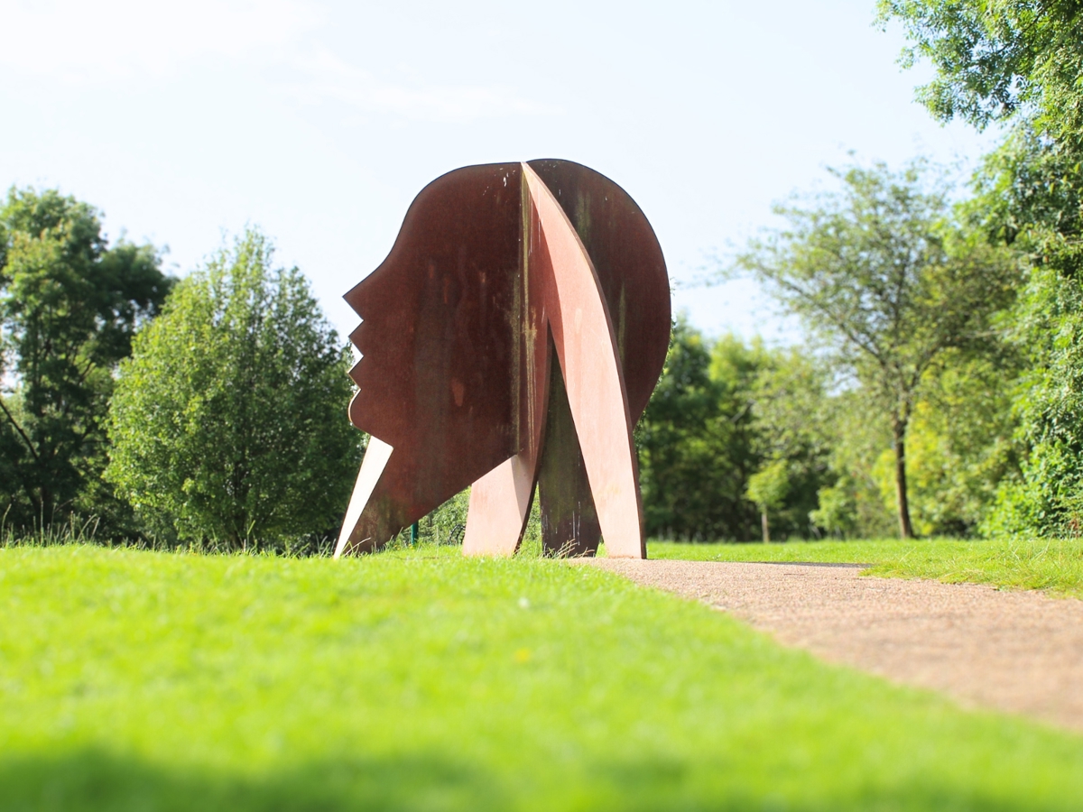 a large metal head made of metal, it is a copper colour as you walk around the piece the head becomes almost 3D as a second head is slotted through the middle of the first
